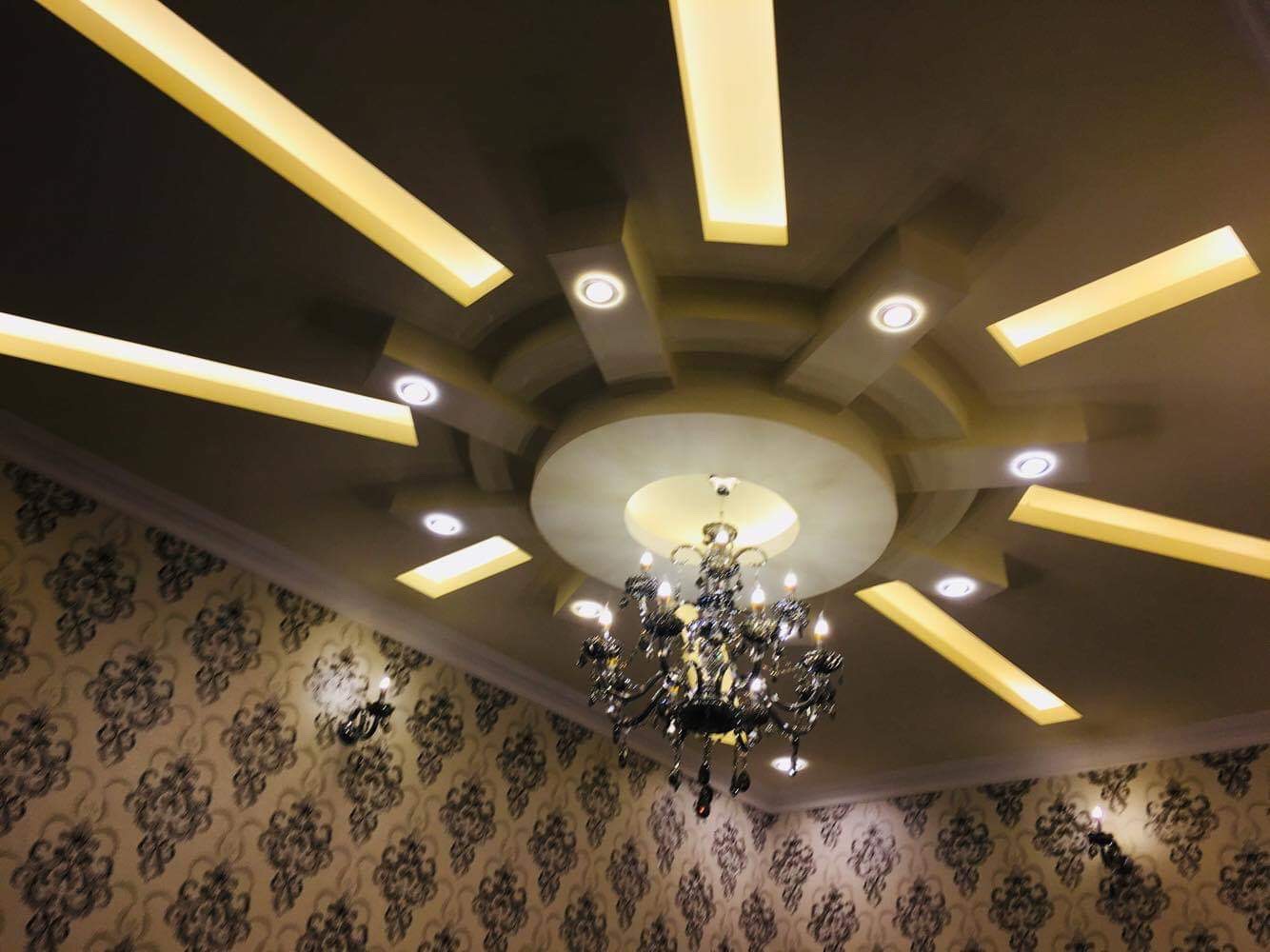 Multi-level gypsum board ceiling with integrated LED cove lighting radiating from a central chandelier fixture