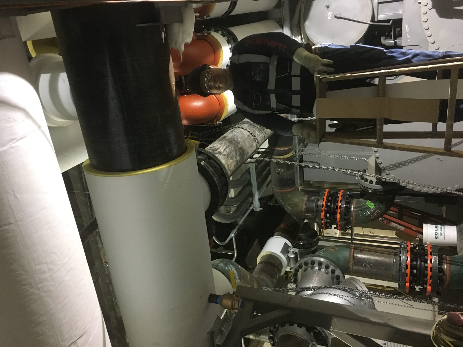 Technician installing insulation on chilled water pipework inside an industrial plant room